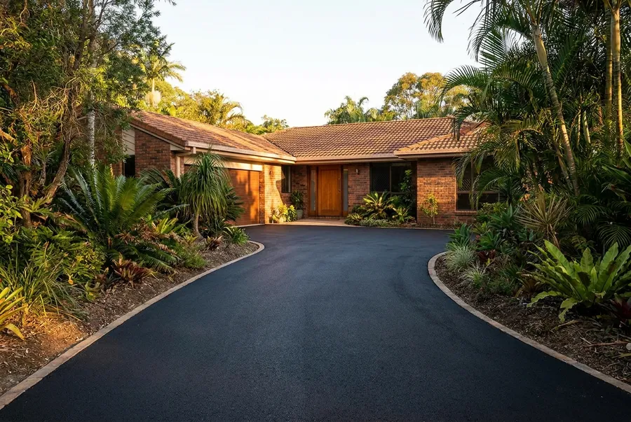New asphalt driveway curving past established gardens